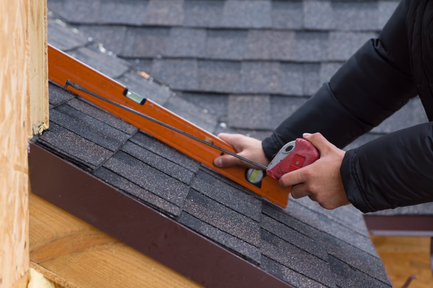 Roofer holding a tape measure and spirit level in his hands over newly installed tiles on a new build wooden house