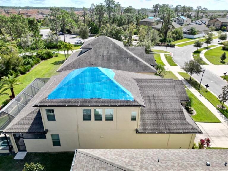 House with a roof partially covered by a blue tarp