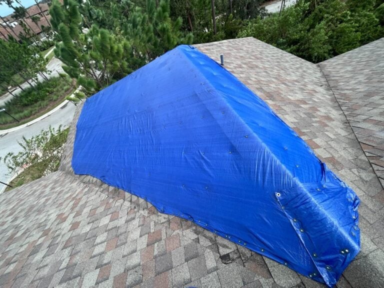 House with a roof partially covered by a blue tarp due to storm damage