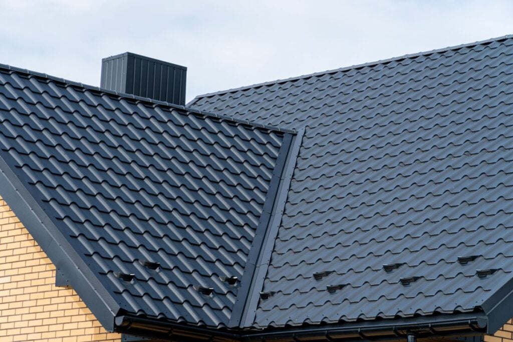 Dark grey metal roof tiles on a modern house with chimney and light brick wall