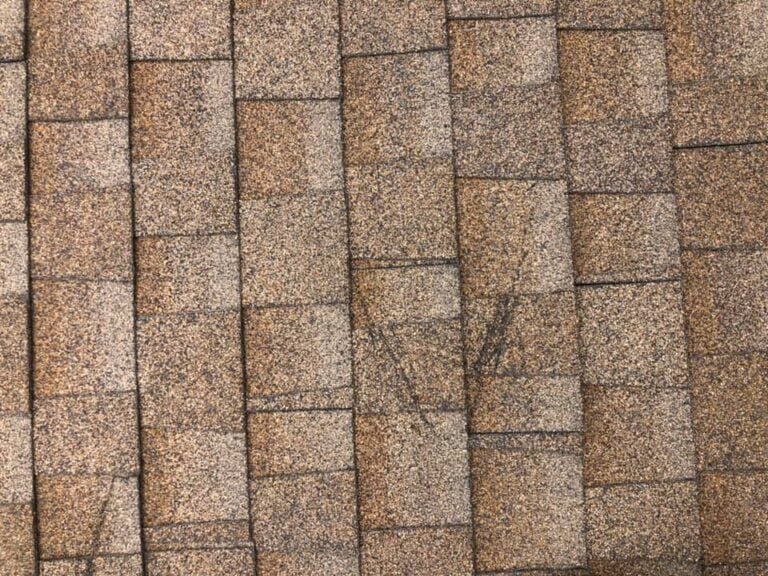 A close-up view of brown asphalt roof shingles arranged in overlapping rows, with a textured and slightly weathered appearance.