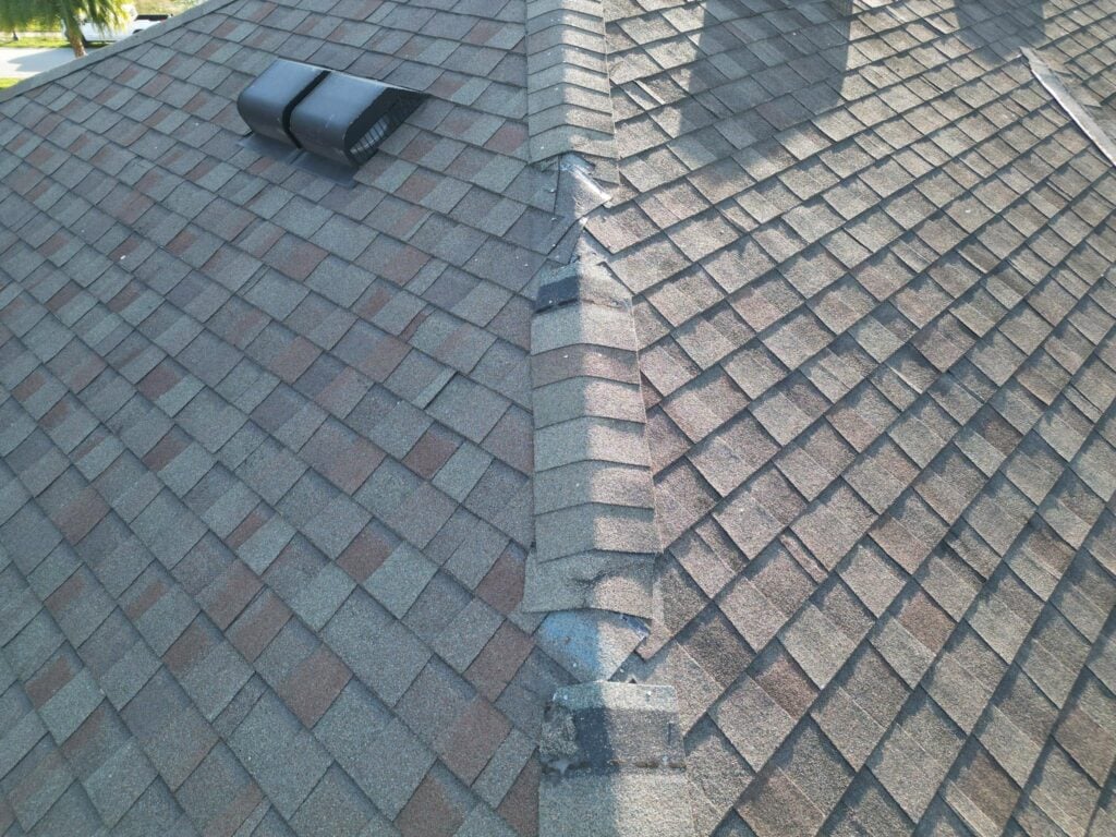 A close-up view of a shingled roof shows the ridge with overlapping shingles and two black roof vents. Homeowners often overlook this area, which can lead to common mistakes during roof insurance claims. The shingles are a mix of brown and gray tones.
