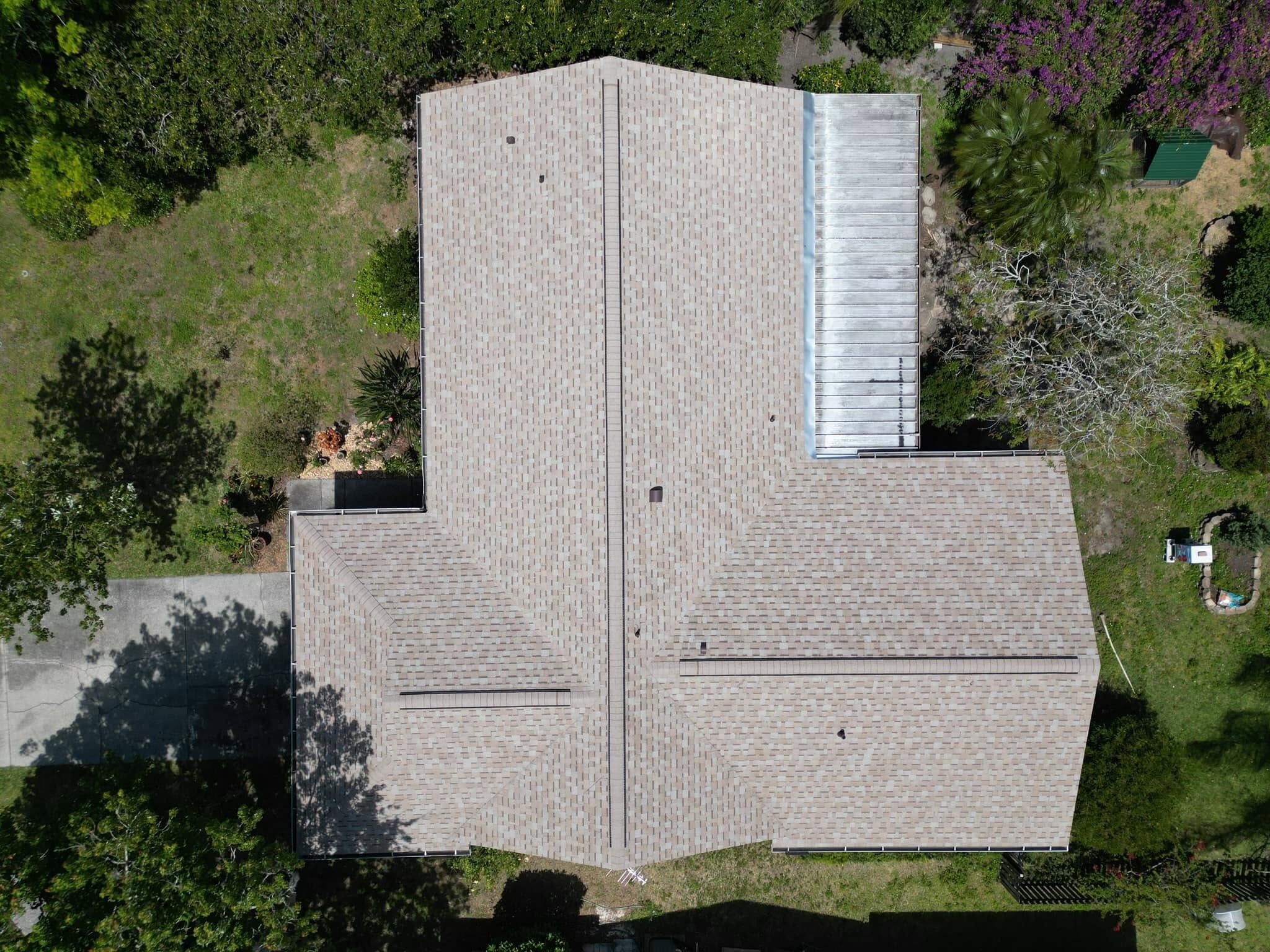 Aerial view of a light brown, shingle-roofed house surrounded by green trees and grass, with a driveway on the left side and a small shed in the backyard—a common setting for homeowners mistakes or insurance claim errors.