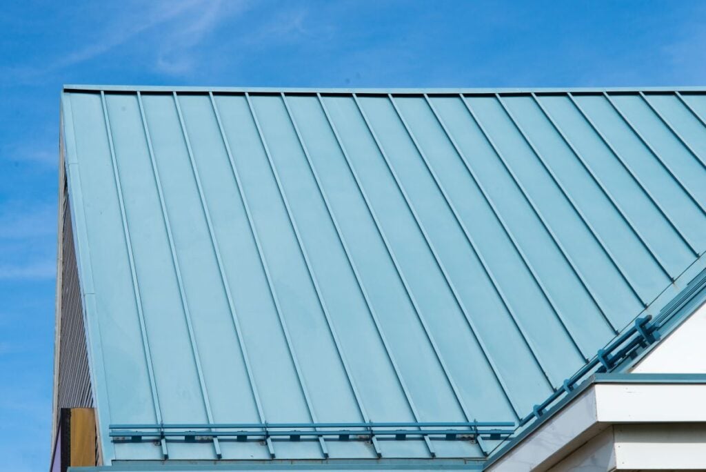 A close-up view of a modern blue metal sloped roof with vertical seams against a clear blue sky. The image highlights its clean, geometric lines—perfect inspiration for a homeowner’s guide on choosing the right option among various metal roof types.