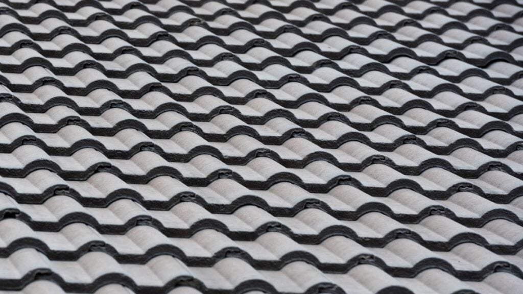 Close-up view of a wavy, repeating pattern of black and gray roof tiles arranged in neat, diagonal rows, highlighting the geometric surface and the tile roof durability seen in quality installations.