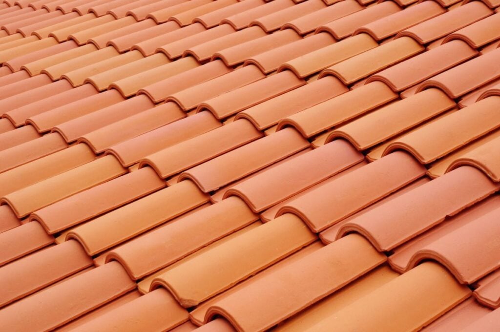 Close-up view of a roof covered with overlapping, reddish-orange clay tiles arranged in a repeating, wavy pattern—proper tile roof maintenance can help preserve this classic look and extend your tile roof lifespan.