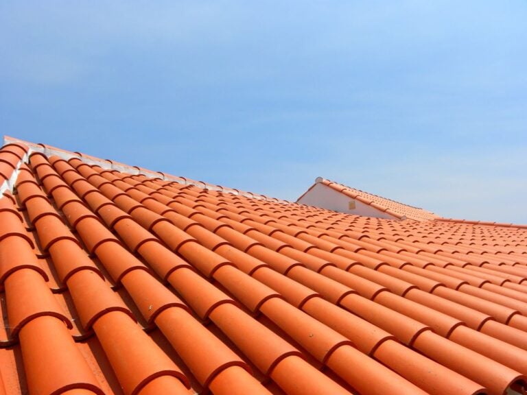 A close-up view of red-orange clay roof tiles on slanted rooftops under a clear blue sky.
