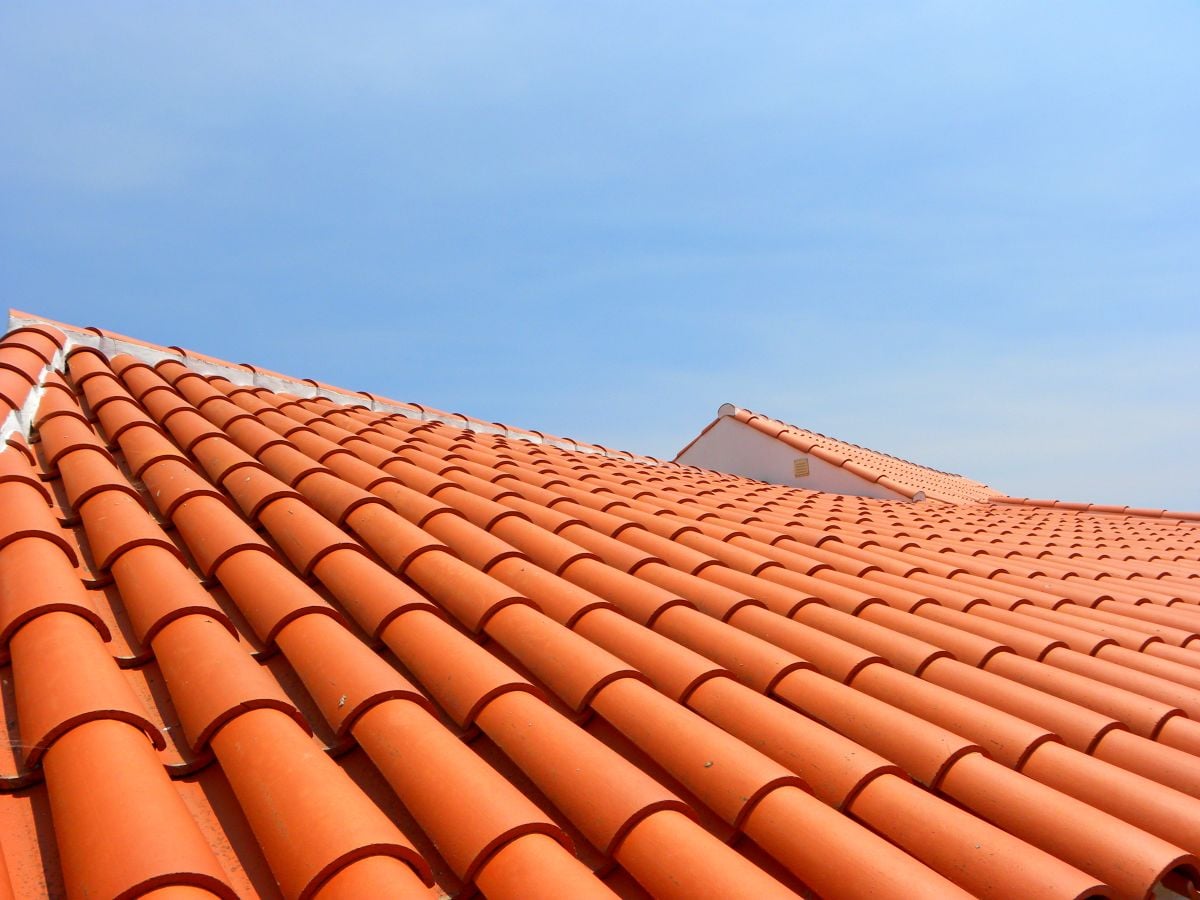A close-up view of red-orange clay roof tiles on slanted rooftops under a clear blue sky.
