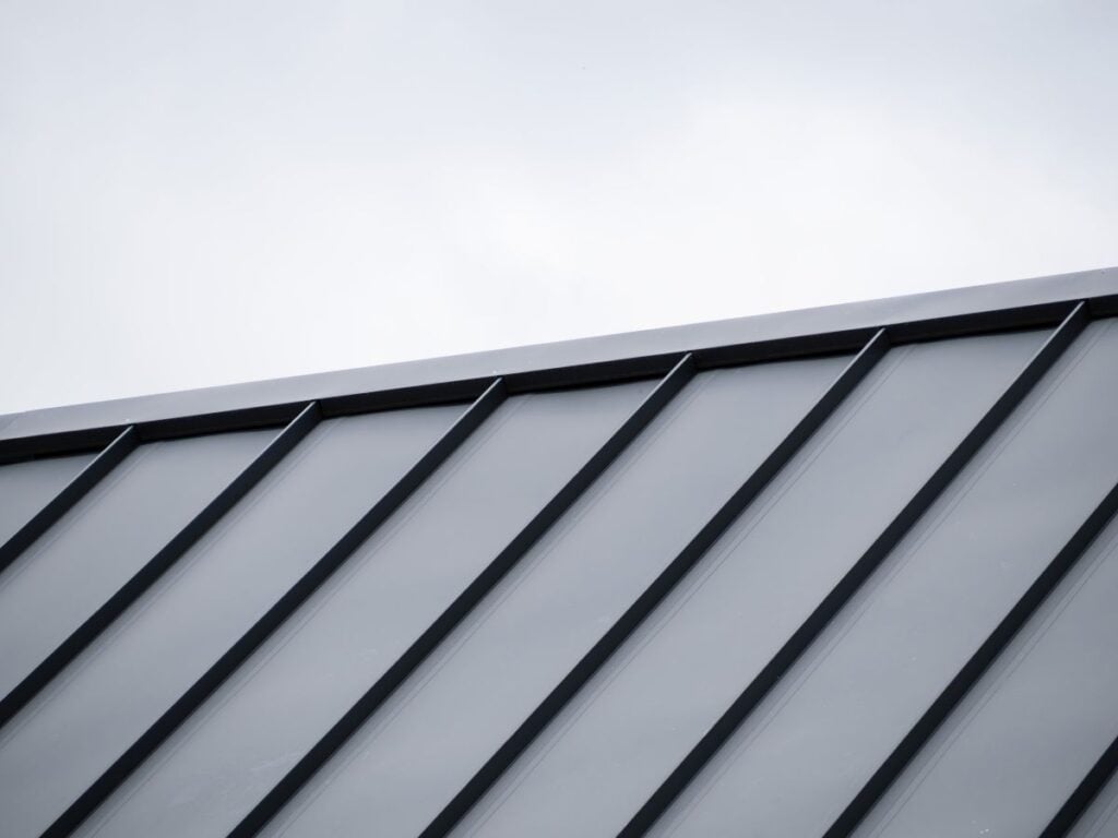Close-up of a modern metal roof with vertical black seams and panels, shown at an angle against a cloudy, light gray sky—an ideal visual for any homeowner’s guide to choosing the right option among various metal roof types.