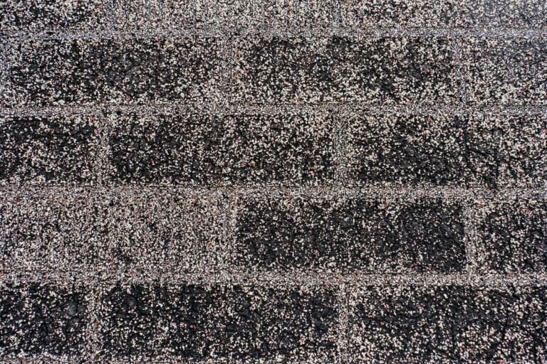 Close-up of dark asphalt roof shingles with a textured surface, featuring horizontal rows and light-colored granules scattered across the surface—a common sign of granular loss on roof and one of the early roof warning signs.