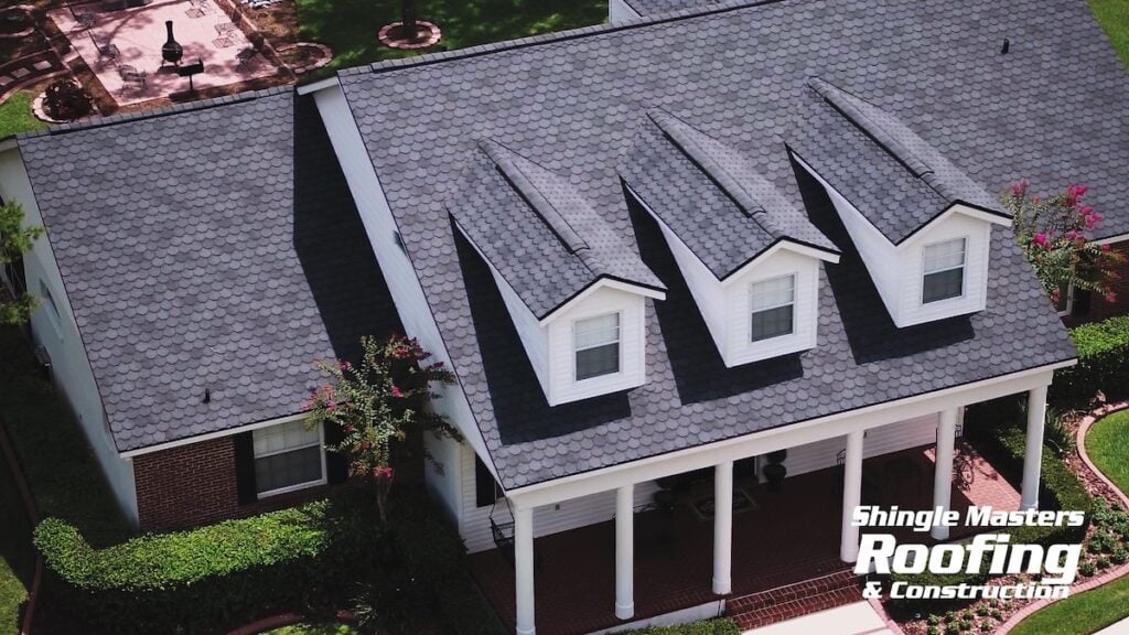 Aerial view of a Florida home with a dark shingle roof showcasing the best shingles, three dormer windows, white columns, and a well-maintained yard; "Shingle Masters Roofing & Construction" logo is in the bottom right corner.