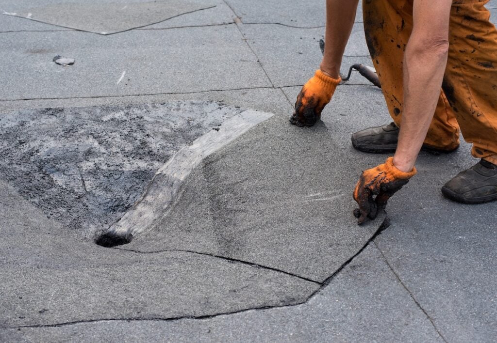 Roofer doing repair roof drain. Flat roof installation. Heating and melting bitumen roofing felt. Flat roof repairing with roofing felt. Professional master , making waterproofing.