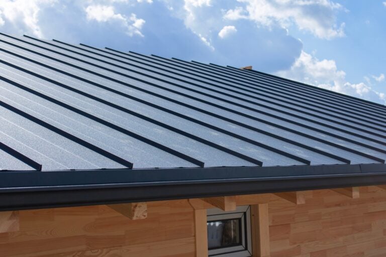 Dark gray standing seam metal roof and black gutter system on a building with natural wooden log walls for exterior building materials. Residential construction and home improvement