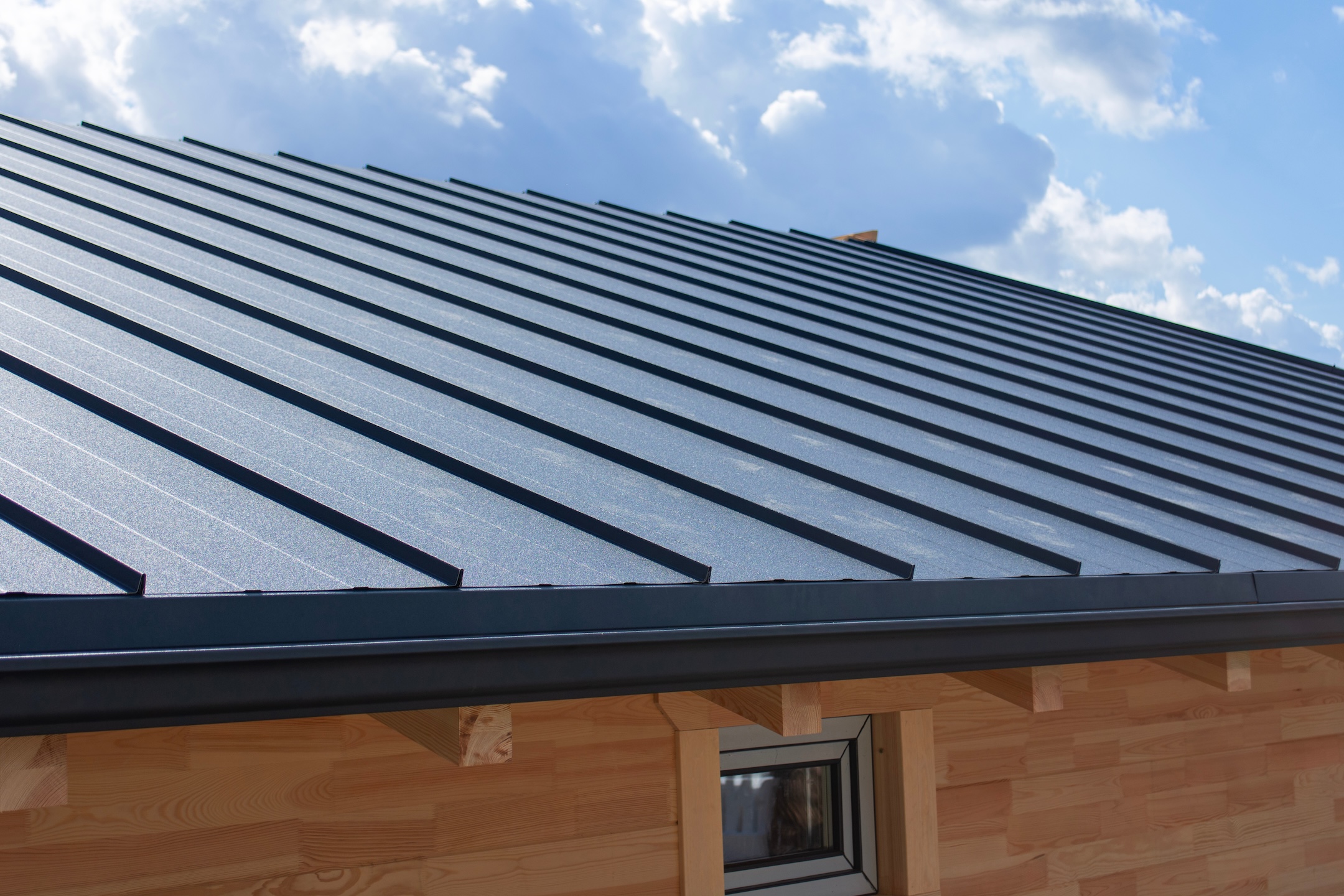 Dark gray standing seam metal roof and black gutter system on a building with natural wooden log walls for exterior building materials. Residential construction and home improvement