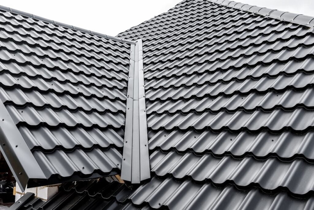 Close-up view of a dark gray metal tile roof with overlapping panels and a central ridge, photographed on a cloudy day—an excellent choice for homeowners seeking long-term value.