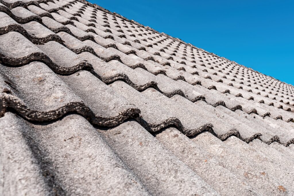 Close-up view of a gray, wavy concrete tile roof under a clear blue sky, showing the repetitive pattern and texture of the roofing material.