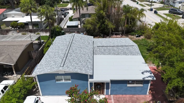 Aerial view of a blue single-story house with a gray shingle roof, white trim, and a red driveway, surrounded by palm trees and neighboring homes in Bradenton fl