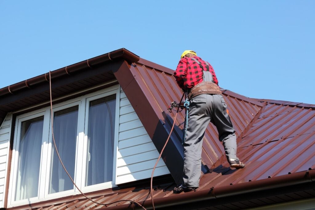 roofer builder worker with pulverizer spraying paint on metal sheet roof