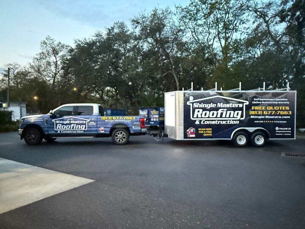 A Shingle Masters Roofing & Construction truck with a matching trailer is parked on a driveway, both prominently displaying company branding, phone number, website, and QR code. This professional setup assures homeowners of quality service as they consider their shingle roof cost options. Trees and houses are visible in the background.