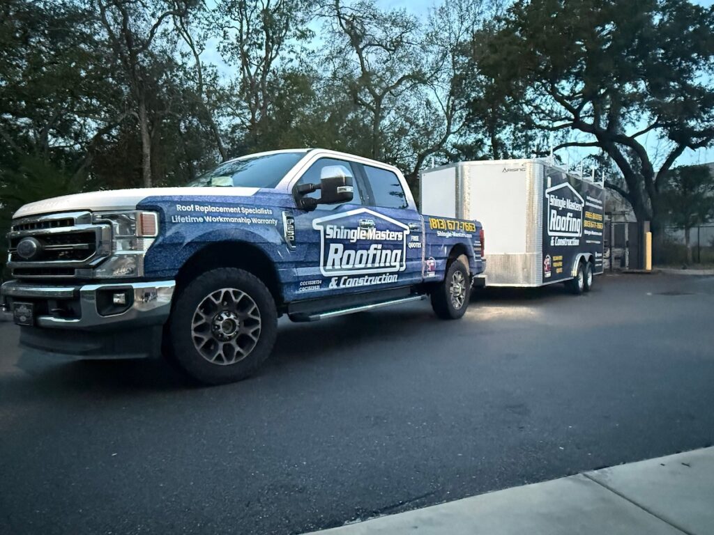 A blue ShingleMasters Roofing & Construction truck is parked with an attached trailer