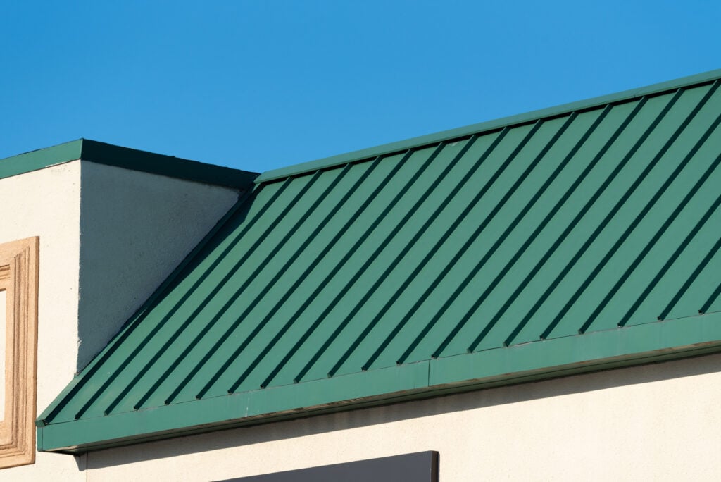 galvalume vs aluminum roof A green Galvalume roof with vertical ridges tops a beige building, set against a clear blue sky.