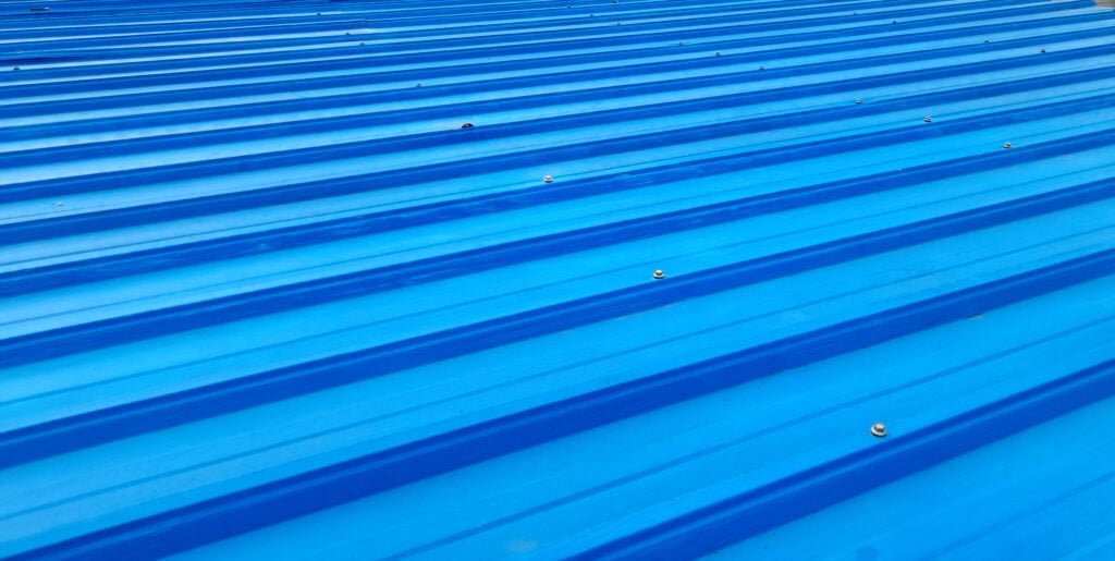 galvalume vs aluminum roof Bright blue corrugated metal roofing with visible screws, viewed at an angle. The repetitive ridges create parallel lines across the surface, typical of a durable aluminum roof.